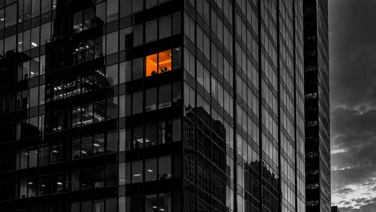 Fachada de torre de vidro em preto e branco com uma única janela iluminada em laranja entre janelas escuras